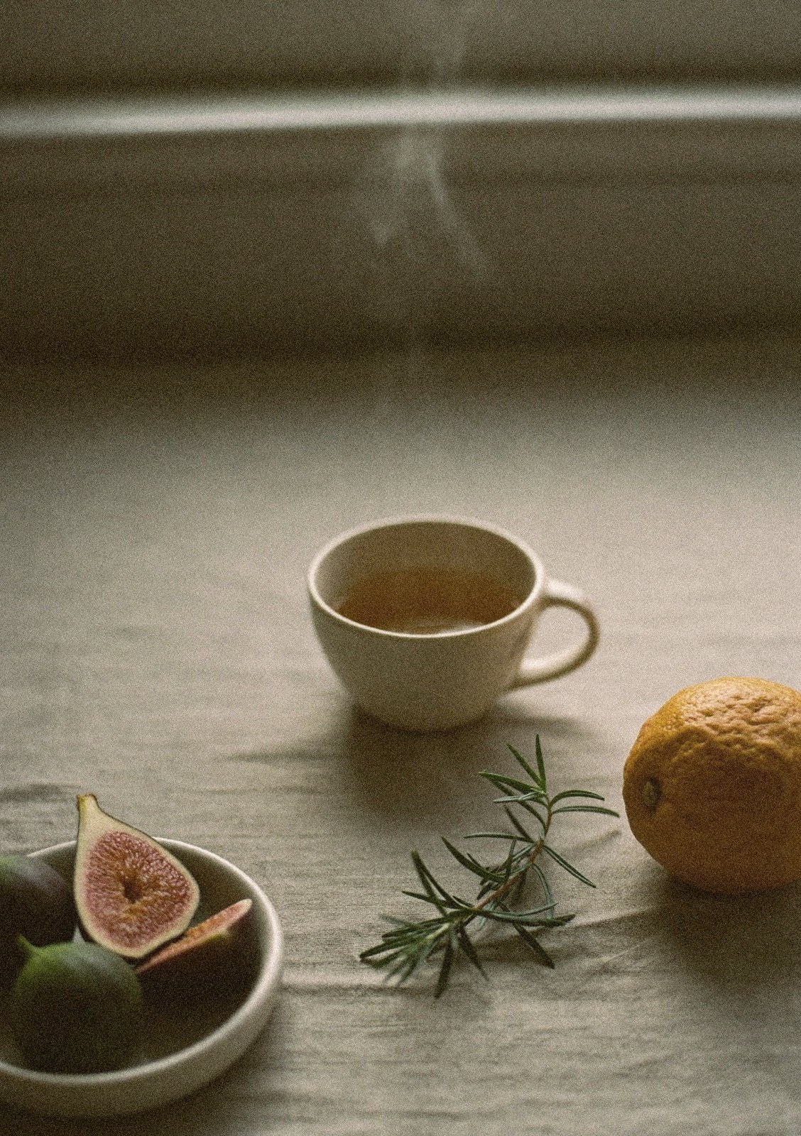 Steaming cup of herbal tea with figs, citrus, and rosemary on a linen cloth